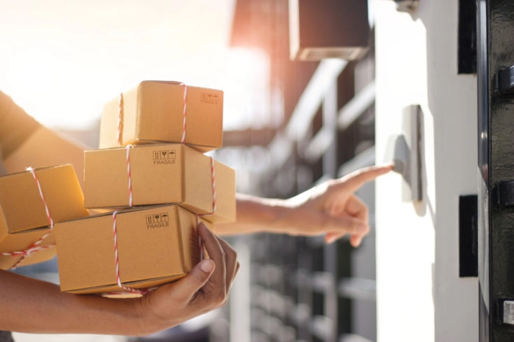 Delivery man holding parcel boxes and ring the doorbell on the client's door in the morning background.