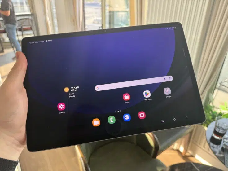 Samsung Galaxy Tab S10 in der Hand mit Stuhl im Hintergrund